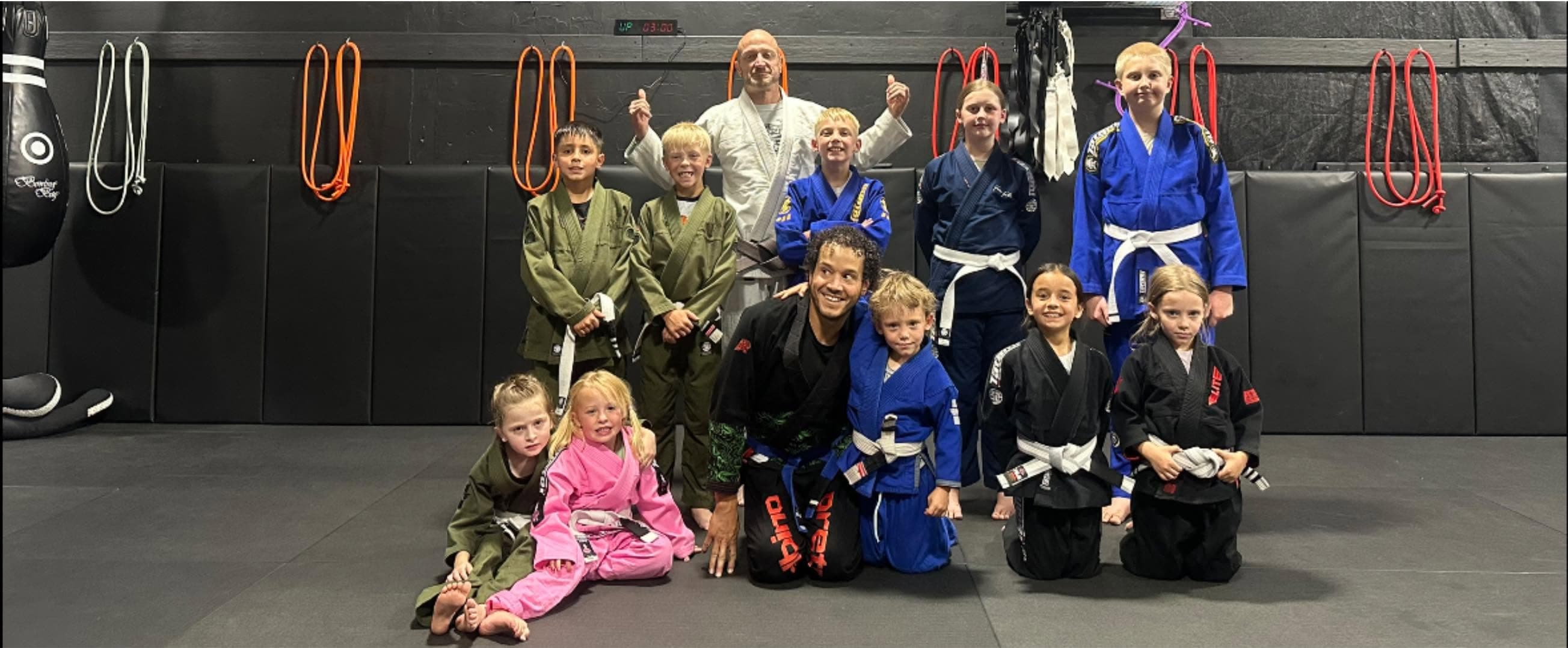 Children and adults in gis posed together on the mat after a Jiu-Jitsu class